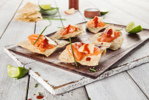 An photo of raw salmon canapes served on toasted flat-bread atop a white timber table