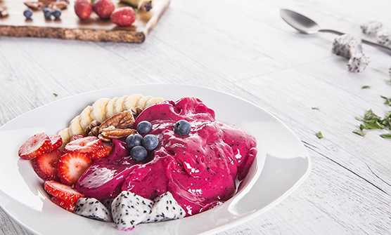 A healthy fruit bowl made from Pink Pitaya (Dragonfruit), topped with blueberries, bananas, strawberries and nuts.