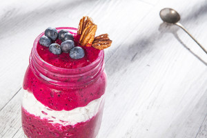 A glass of fruit smoothie made from Pink Pitaya (Dragonfruit), made with coconut cream and topped with blueberries and nuts.