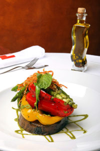 A photo of a gourmet eggplant steak with other vegetables piled on top on a white service restaurant table