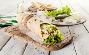 Bright high-key image of a healthy flat-bread salad wrap being prepared and served on a weathered wooden food board